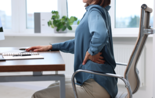 woman sitting in a office chair infront of a desk holding her lower back