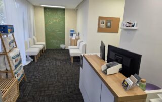 Reception desk and waiting area at Northbridge Chiropractic in Perth featuring cream boucle chairs, a green chalkboard welcome wall, and health products on display.