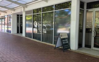 Street-level exterior view of Northbridge Chiropractic clinic in Perth with the clinic name on the window, a walk-ins welcome A-frame sign on the footpath, and a covered arcade entrance.