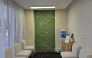 Patient waiting area at Northbridge Chiropractic in Perth with cream boucle chairs, a green chalkboard feature wall with wellness quotes, and a water dispenser station.