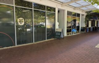 Angled street view of Northbridge Chiropractic clinic frontage in Perth showing the clinic logo on the shopfront window and a walk-ins welcome sign on the footpath beneath a covered arcade.