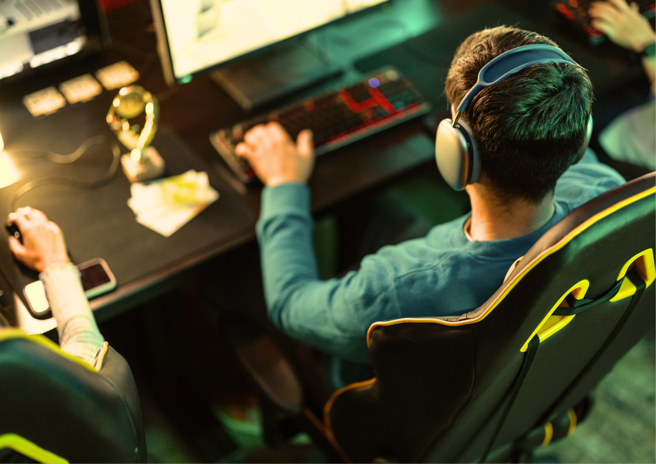 Young man wearing headphones sitting in a gaming chair at a computer desk in a dimly lit room, illustrating prolonged sedentary posture and neck strain associated with extended screen time and gaming.